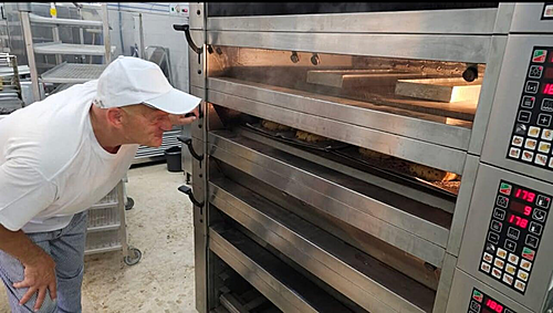 **Descripción de la imagen SEO amigable:**  "El dueño y maestro panadero de la panadería supervisa la preparación de productos frescos en el horno, combinando tradición y calidad en cada elaboración."